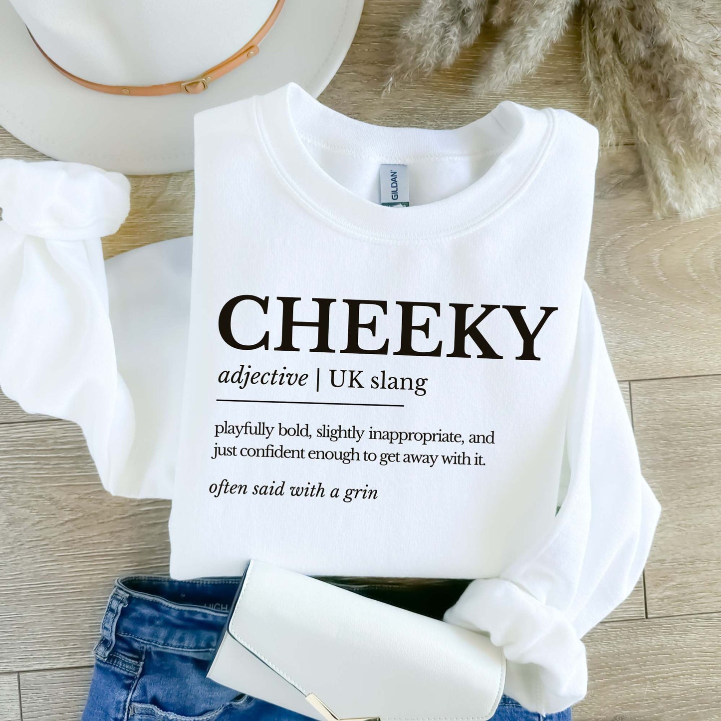 White sweatshirt with 'CHEEKY' definition text on a wooden surface