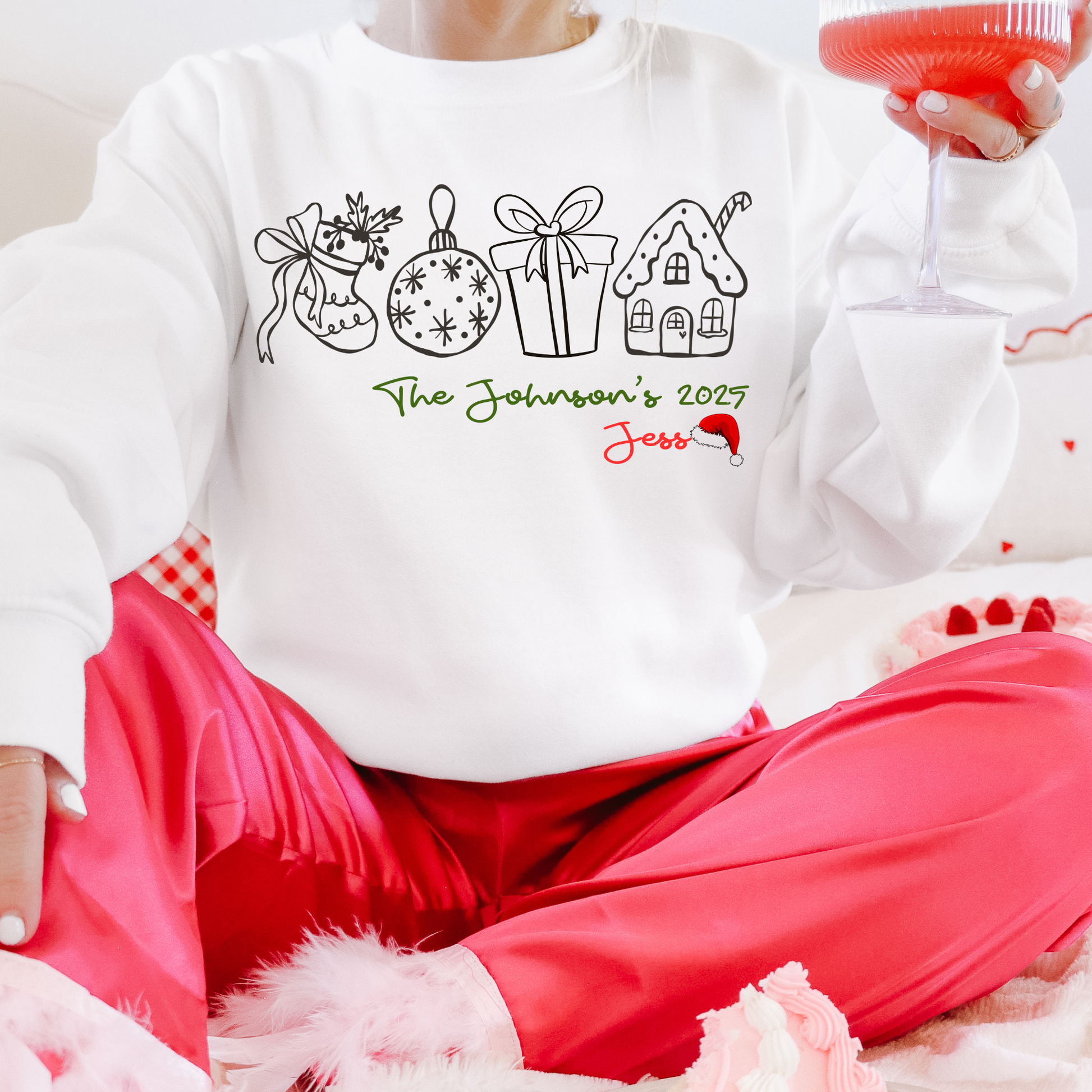 Person wearing a white sweatshirt with Christmas-themed designs and text, sitting on a pink couch.