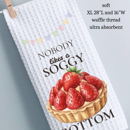 Waffle-textured towel with strawberry design and text, hanging on a clothespin against a light gray background.