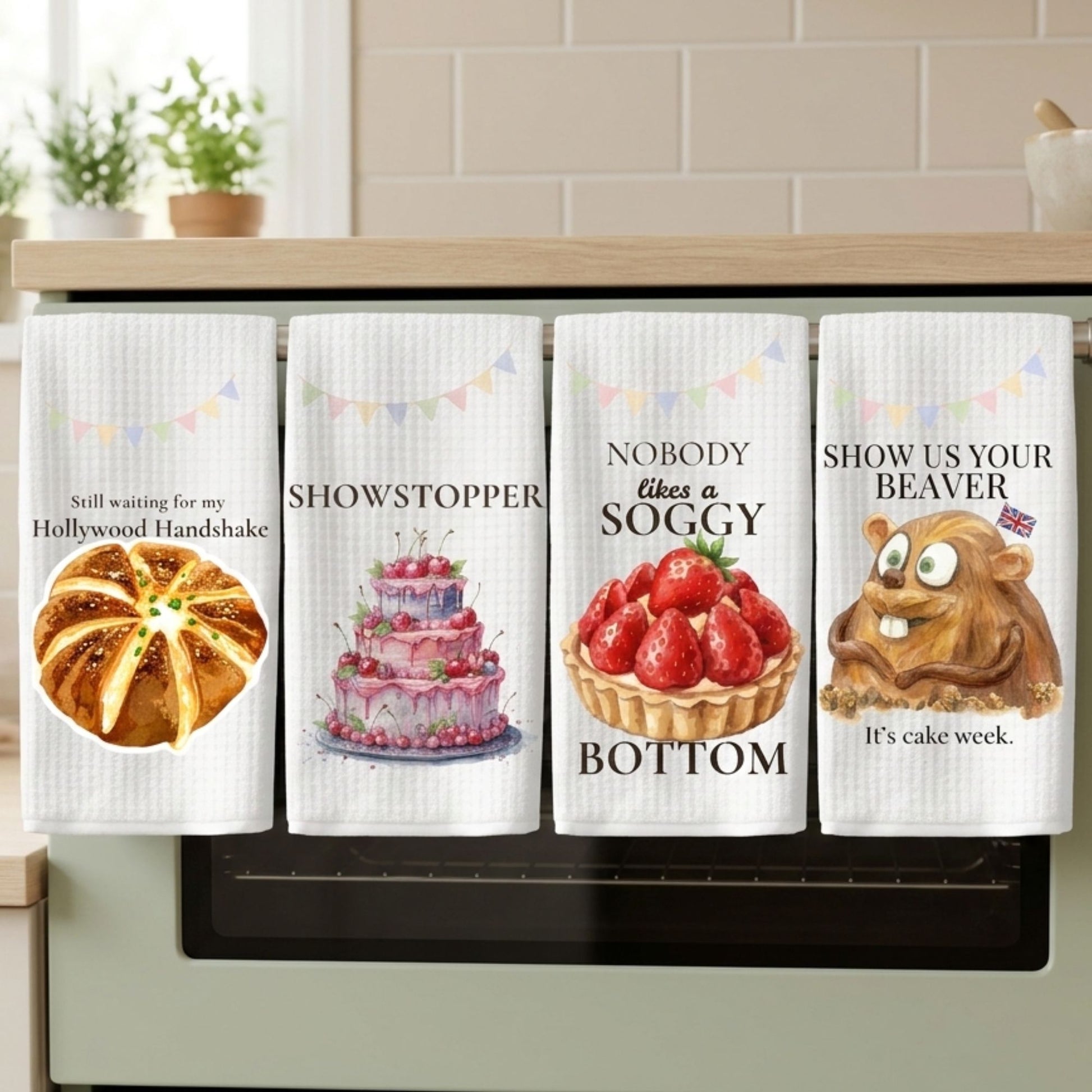 Four kitchen towels with humorous prints hanging on a kitchen cabinet.