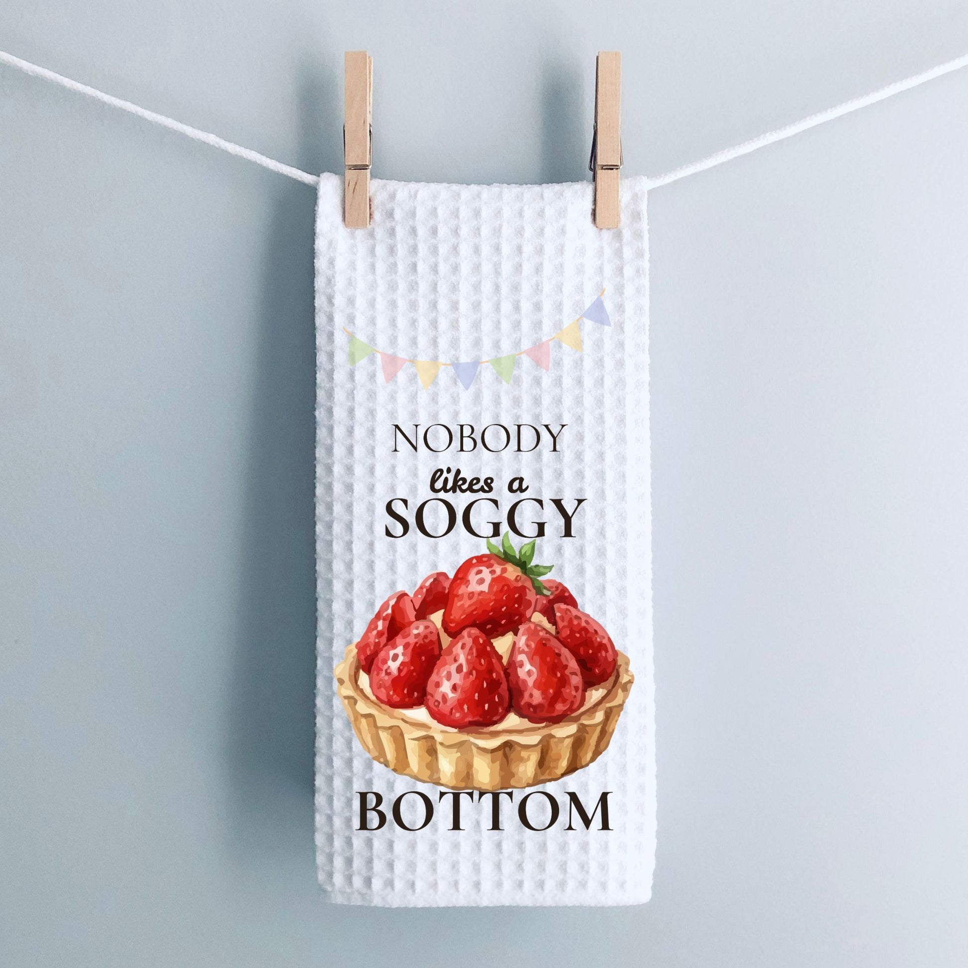 Tea towel with strawberry tart design and text hanging on a line.