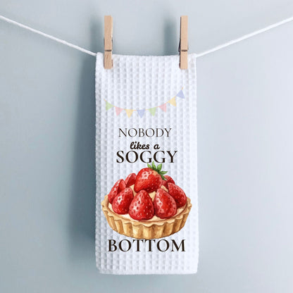 Tea towel with strawberry tart design and text hanging on a line.