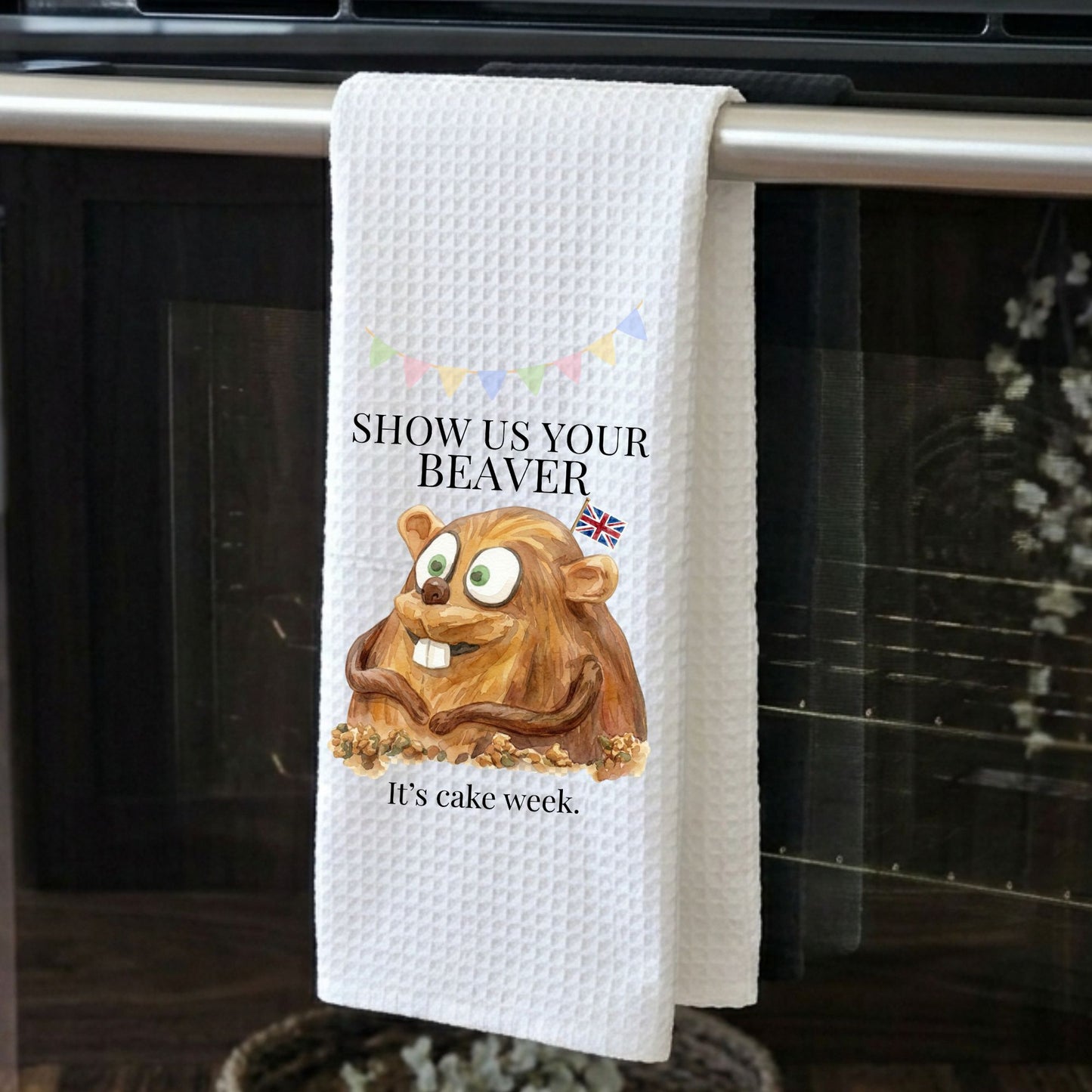 Kitchen towel with a cartoon beaver and text hanging on an oven handle.