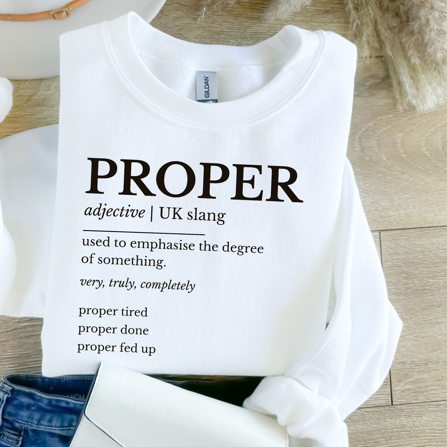 White sweatshirt with 'PROPER' definition text on a wooden surface