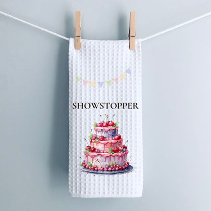 Waffle text towel with a cake design and 'SHOWSTOPPER' text, hanging on a line.