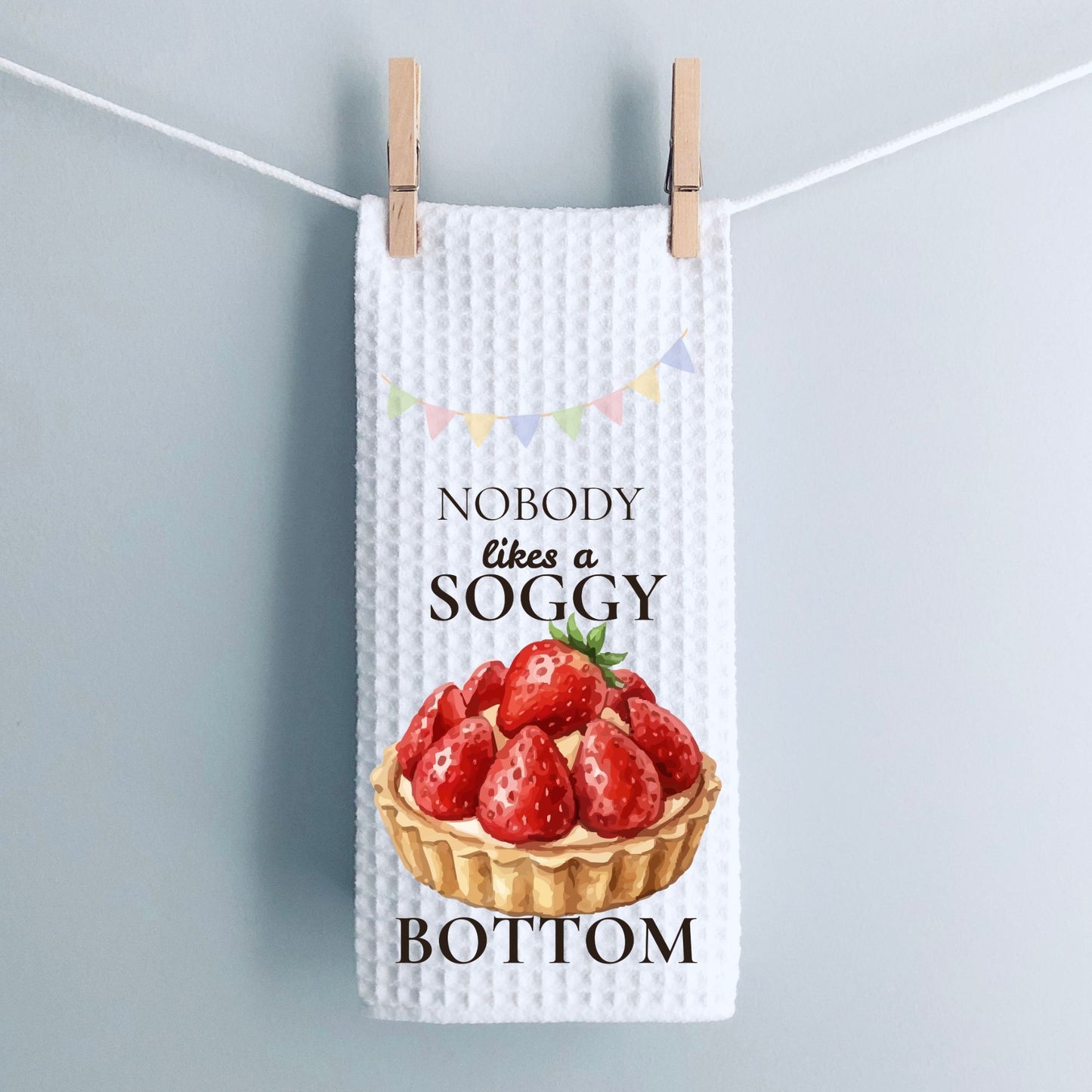 Waffle-textured tea towel with strawberry tart design and text on a light gray background