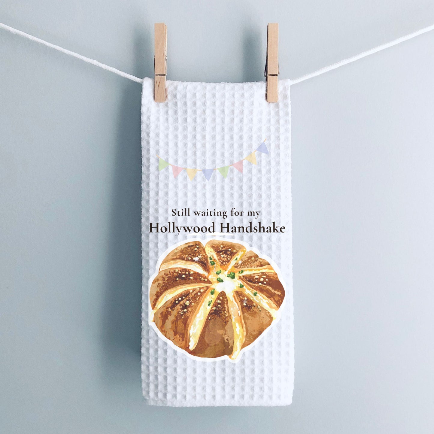Waffle-textured towel with bread graphic and text 'Still waiting for my Hollywood Handshake' on a gray background.