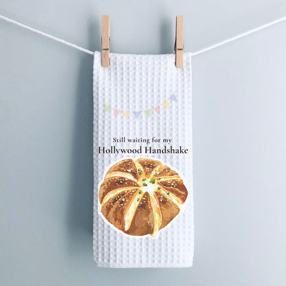 Waffle-textured towel with bread graphic and text 'Still waiting for my Hollywood Handshake' on a gray background.