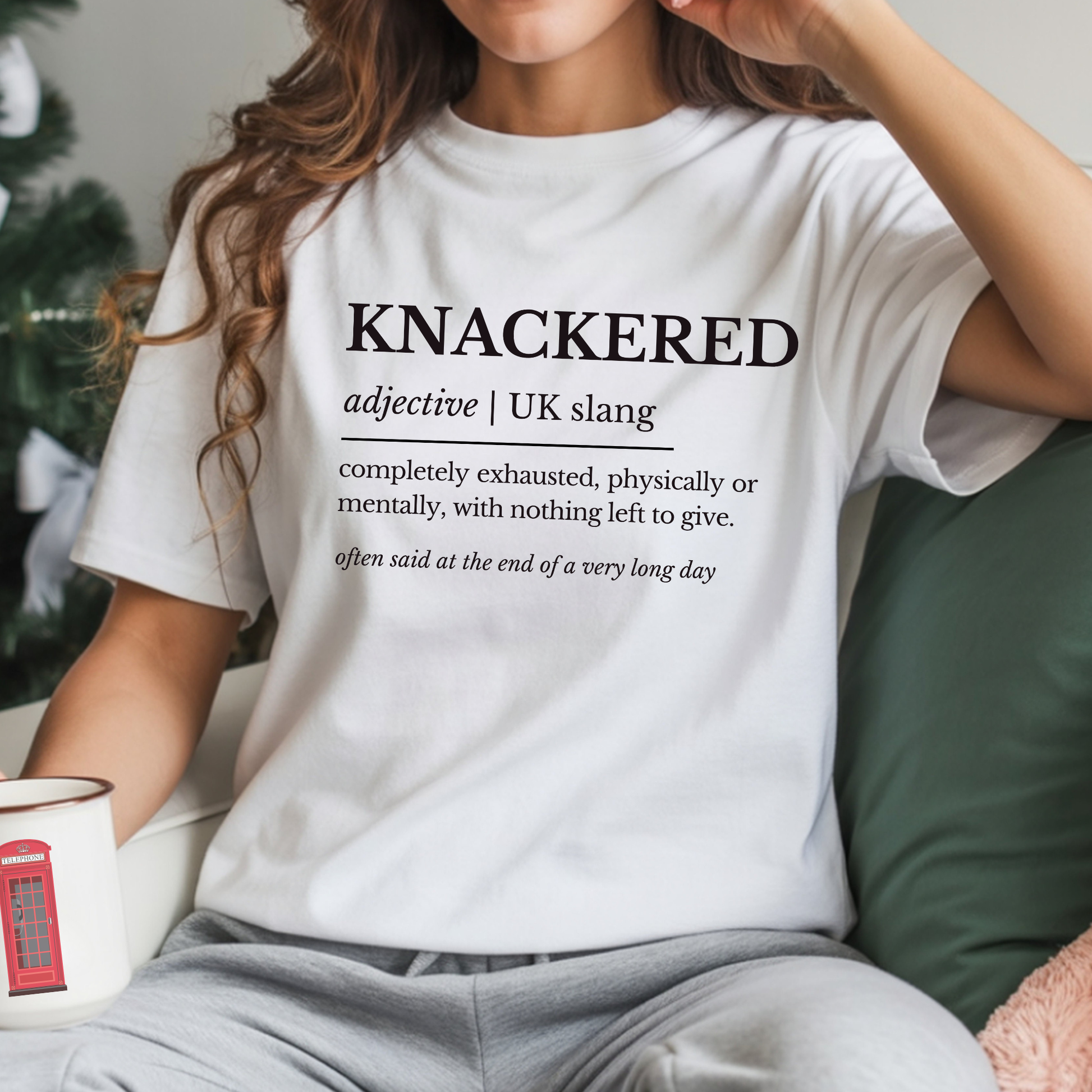 Person wearing a white t-shirt with the word 'KNACKERED' and its definition, sitting on a couch.