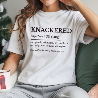 Person wearing a white t-shirt with the word 'KNACKERED' and its definition, sitting on a couch.