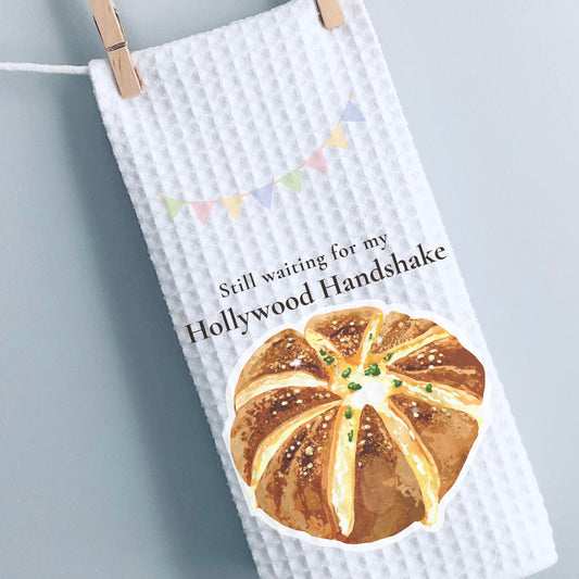 White towel with bread graphic and text 'Still waiting for my Hollywood Handshake' on a gray background