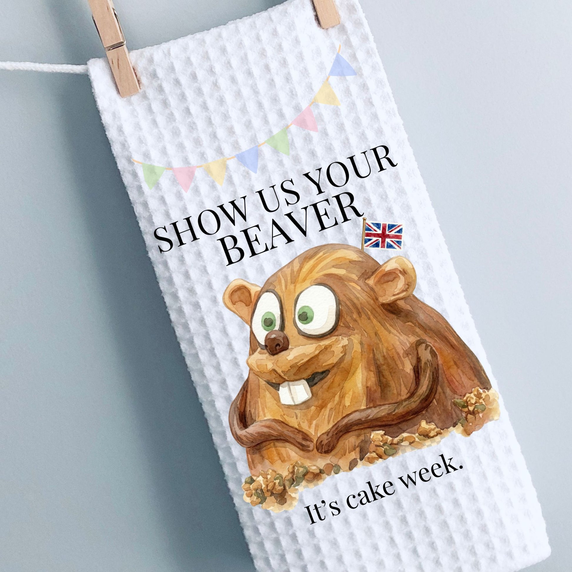 White towel with cartoon beaver and text 'Show us your beaver, it's cake week.' hanging on a line.