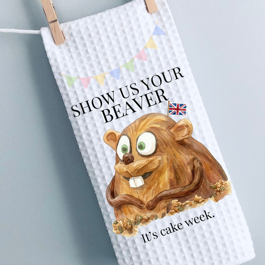 White towel with cartoon beaver and text 'Show us your beaver, it's cake week.' hanging on a line.